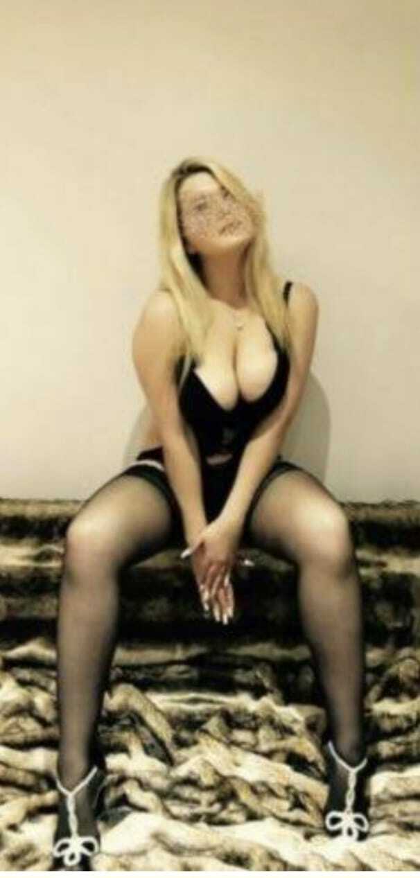 Woman in black lingerie seated on stairs, legs apart, hands clasped near knees, looking upward.